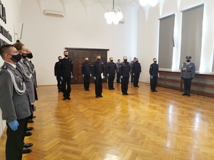 nowi policjanci podczas uroczystości ślubowania, w tle widać sztandar policji oraz osoby uczestniczące w uroczystości i komendanta