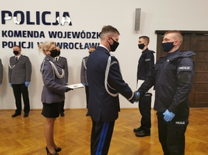 nowi policjanci podczas uroczystości ślubowania, w tle widać sztandar policji oraz osoby uczestniczące w uroczystości i komendanta