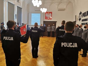 nowi policjanci podczas uroczystości ślubowania, w tle widać sztandar policji oraz osoby uczestniczące w uroczystości i komendanta