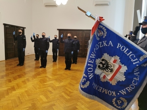 nowi policjanci podczas uroczystości ślubowania, w tle widać sztandar policji oraz osoby uczestniczące w uroczystości i komendanta