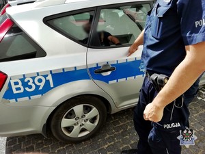 na parkingu stoi radiowóz a w nim zatrzymany mężczyzna, obok stoją policjanci