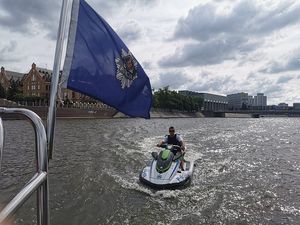 umundurowany funkcjonariusz policji pływający na skuterze wodnym, w tle flaga z napisem policja