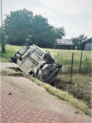 Zdjęcie przedstawia samochód osobowy, który leży na dachu w przydrożnym rowie