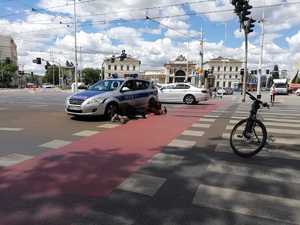 radiowóz blokujący ruch na skrzyżowania, obok ludzie próbujący wydostać kaczkę spod auta,