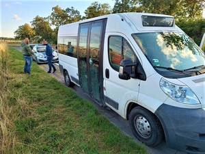 Na zdjęciu widać bus, za którym stoi radiowóz. Pomiędzy tymi pojazdami stoi dwóch mężczyzn.