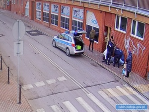 Zdjęcia przedstawiają ulicę, przy której policjanci udzielają poszkodowanej kobiecie pomocy. Na ulicy stoi oznakowany radiowóz