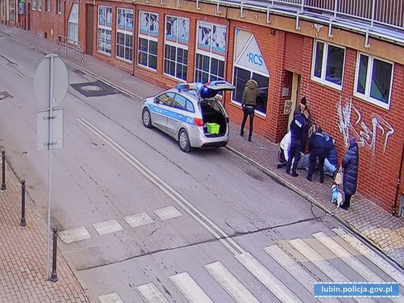 Zdjęcia przedstawiają ulicę, przy której policjanci udzielają poszkodowanej kobiecie pomocy. Na ulicy stoi oznakowany radiowóz