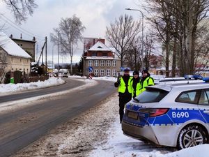 Przy drodze radiowóz, za nim trójka policjantów w kamizelkach odblaskowych, wkoło śnieg