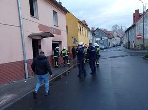 Na zdjęciu policjanci i strażacy stojący przed budynkiem, w którym wybuchł pożar.