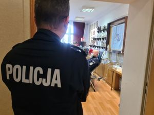 Na zdjęciu na pierwszym planie policjant stojący tyłem, do robiącego zdjęcie. W tle policjant w maseczce siedzący na fotelu któremu pobierana jest krew.