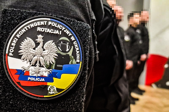 Na zdjęciu plakietka z napisem Polski Kontyngent Policyjny w Ukrainie. W tle policjanci.
