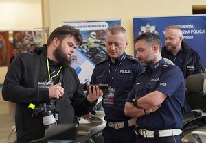 policjanci stojący przy mężczyźnie pokazującym im telefon w pomieszczeniu