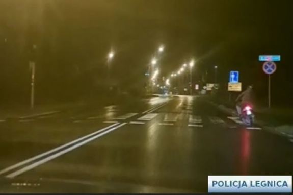 Kadr z filmu motorowerzysta jadący drogą w porze nocnej.