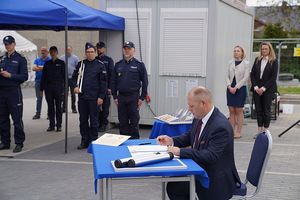 Na zdjęciu mężczyzna podpisujący akt erekcyjny w tle plac budowy z maszynami budowlanymi.