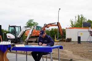 Na zdjęciu Naczelnik Wydziału Inwestycji i Remontów Komendy Wojewódzkiej Policji we Wrocławiu - młodszy inspektor Robert Szady podpisujący akt erekcyjny w tle plac budowy z maszynami budowlanymi.