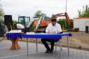 Na zdjęciu Prezes Zarządu firmy CLIMATIC podpisujący akt erekcyjny w tle plac budowy z maszynami budowlanymi.
