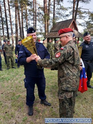 Przewodnik psa służbowego policjant w mundurze odbiera puchar od funkcjonariusza Straży Granicznej.