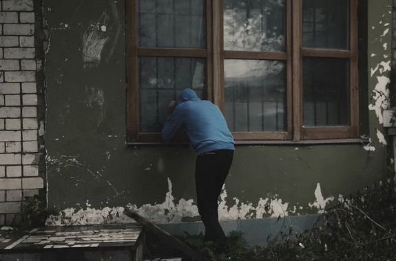 Mężczyzna zaglądający przez okna do budynku. Źródło zdjęcia: Canva