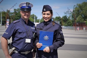 policjantka trzyma granatową teczkę, obok niej stoi policjant w białej czapce