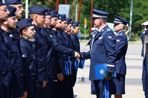 Komendant Wojewódzki Policji we Wrocławiu nadinspektor Dariusz Wesołowski gratuluje poprzez podanie ręki nowo przyjętemu policjantowi stojącemu w dwuszeregu.