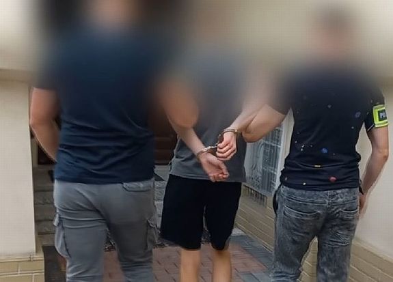 Policjanci w cywilnych ubraniach prowadzą zatrzymanego mężczyznę.