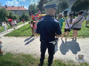 Na pierwszym planie policjant za nim bawiące się dzieci