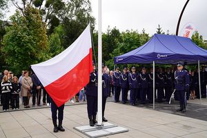 Flaga polski powiewa na maszcie, w tle policjanci.