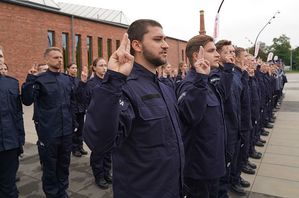 Policjanci stojący w dwuszeregu z uniesionymi dwoma palcami ku górze ślubują.