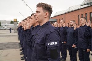 Nowoprzyjęci policjanci stojący w dwuszeregu z uniesionymi dwoma palcami ku górze ślubują.