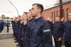 Policjanci stojący w dwuszeregu z uniesionymi dwoma palcami ku górze ślubują.