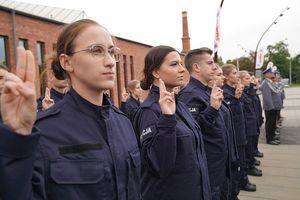 Nowoprzyjete policjantki stojące w dwuszeregu z uniesionymi dwoma palcami ku górze ślubują.