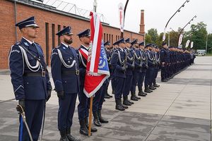 Poczet sztandarowy wraz z nowoprzyjętymi policjantami stojący w szeregu.