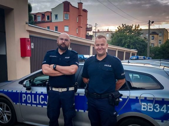 Dwaj policjanci stojący koło radiowozu.