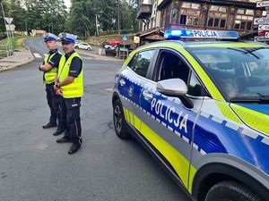 Policjanci ruchu drogowego stojący przy radiowozie i kierują ruchem drogowym