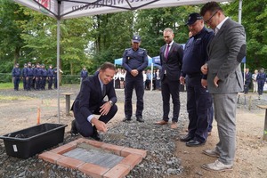 Mężczyzna trzyma kielnię z zaprawą i wmurowuje akt erekcyjny. Obok I Zastępca Komendanta Wojewódzkiego Policji we Wrocławiu wraz z oficjelami.