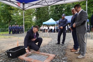 Mężczyzna wmurowuje akt erekcyjny. Obok I Zastępca Komendanta Wojewódzkiego Policji we Wrocławiu wraz z oficjelami.