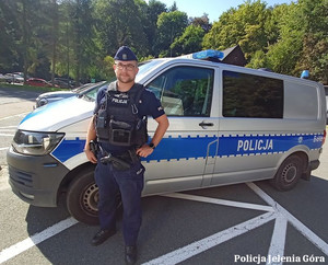 Policjant stojący przed radiowozem.