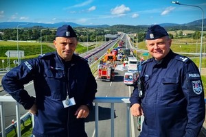 Dwaj policjanci na wiadukcie - w tle  ćwiczenia służb ratowniczych na drodze S-3 z udziałem dolnośląskich policjantów.