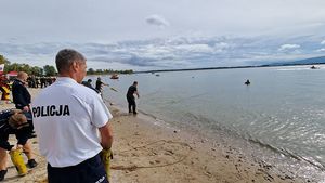 Policjant na brzegu przygląda się akcji ratunkowej przeprowadzanej przez żołnierzy.