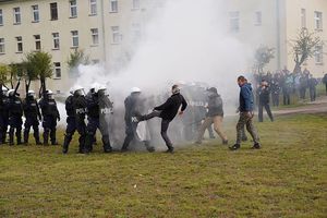 policjanci w białych kaskach i z tarczami stojący na murawie, za nimi dym