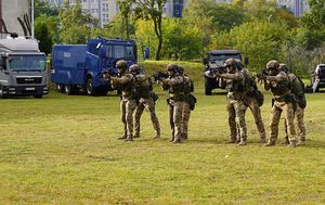 Policjanci w zielonym mundurze z bronią na murawie