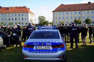 osoby stojące przed policyjnym oznakowanym radiowozem