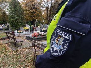 Osoba z naszywką z napisem Komenda Powiatowa Policji w Zgorzelcu na ramieniu, w tle groby