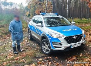 Mężczyzna stojący w lesie przy oznakowanym radiowozie