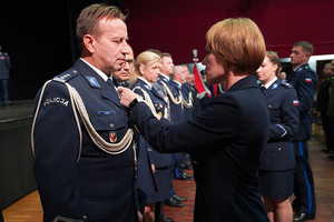 Przedstawicielka Wojewody dolnośląskiego przypina medal policjantowi. W tle pozostali uhonorowani policjanci i policjantki.