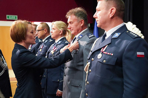 Przedstawicielka Wojewody dolnośląskiego przypina medal policjantowi. W tle pozostali uhonorowani policjanci i policjantki.