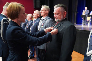 Przedstawicielka Wojewody dolnośląskiego przypina medal mężczyźnie w garniturze. W tle pozostali odznaczeni mężczyźni.