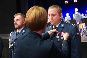 Przedstawicielka Wojewody dolnośląskiego przypina medal policjantowi. Obok stoi odznaczony policjanci.