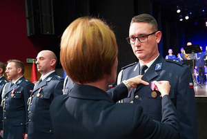 Przedstawicielka Wojewody dolnośląskiego przypina medal policjantowi. W tle pozostali odznaczeni policjanci.