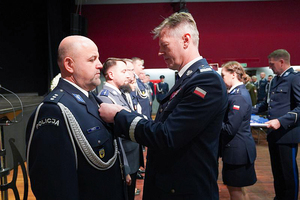 Komendant Wojewódzki Policji we Wrocławiu nadinspektor Dariusz Wesołowski przypina odznaczenie policjantowi stojącemu w szeregu.